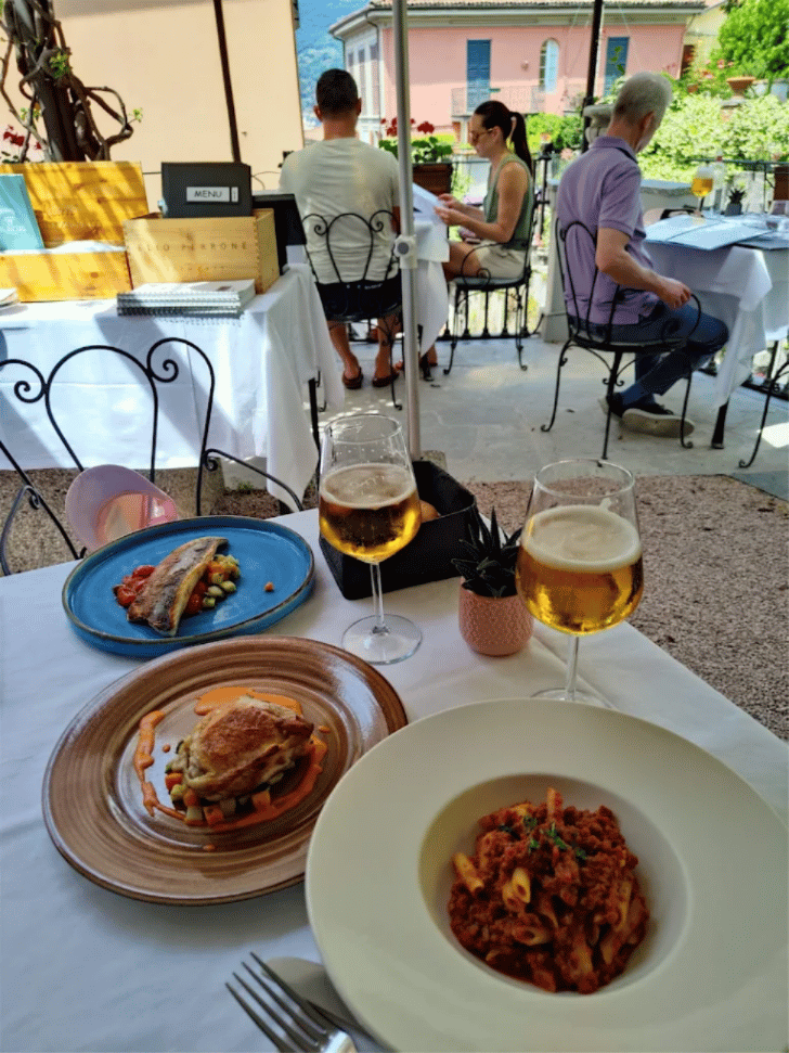Plated dishes and wine on Ristorante Bilacus's shaded terrace in Bellagio