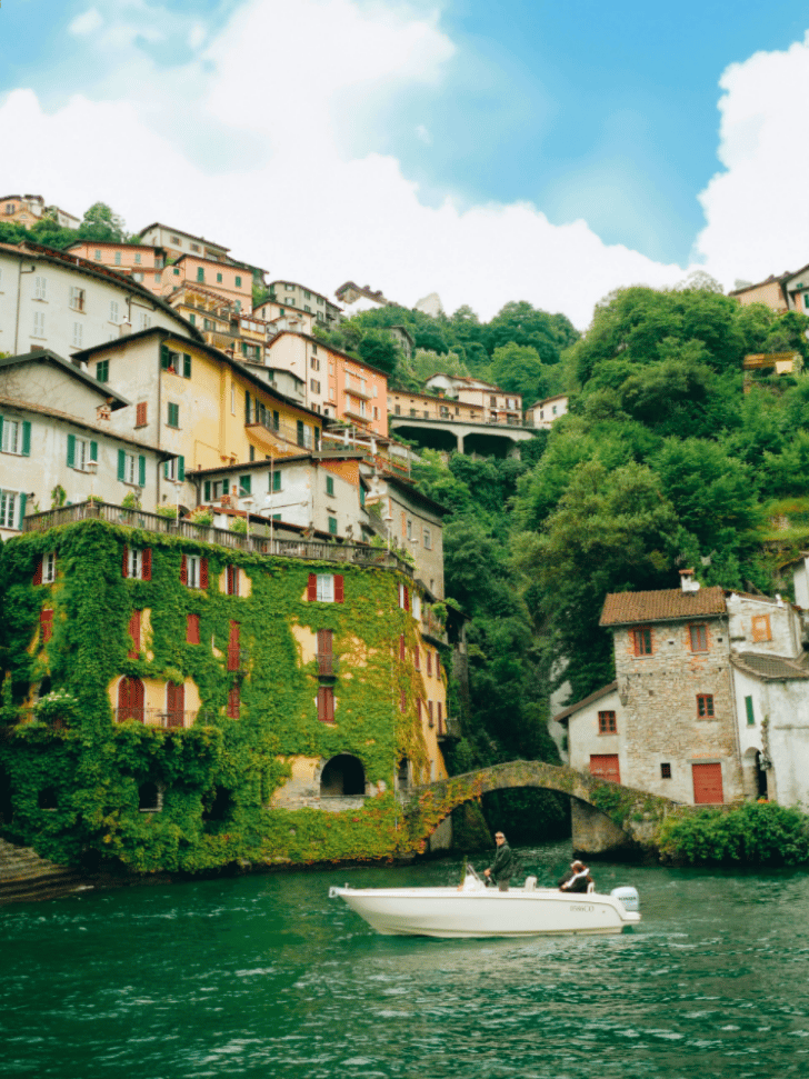 Boat passing under Nesso's ivy-covered stone bridge on Lake Como