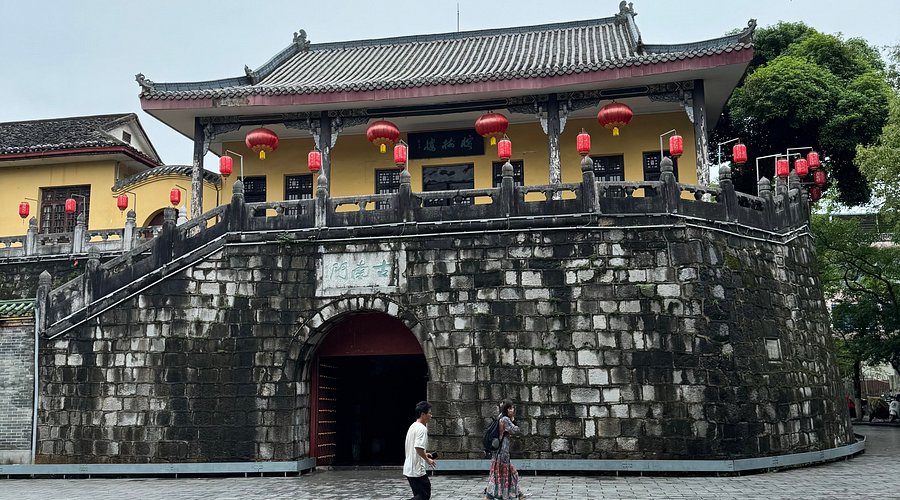 A stone city gate with a tiled roof and hanging red lanterns above a lake