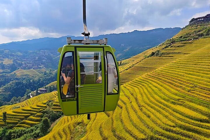 A green cable car gondola crossing above golden rice terraces at Dazhai