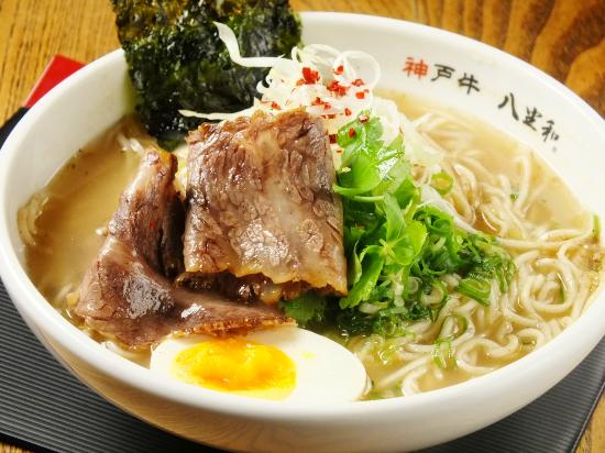 A ramen bowl topped with sliced Kobe beef, spring onion, and a soft-boiled egg