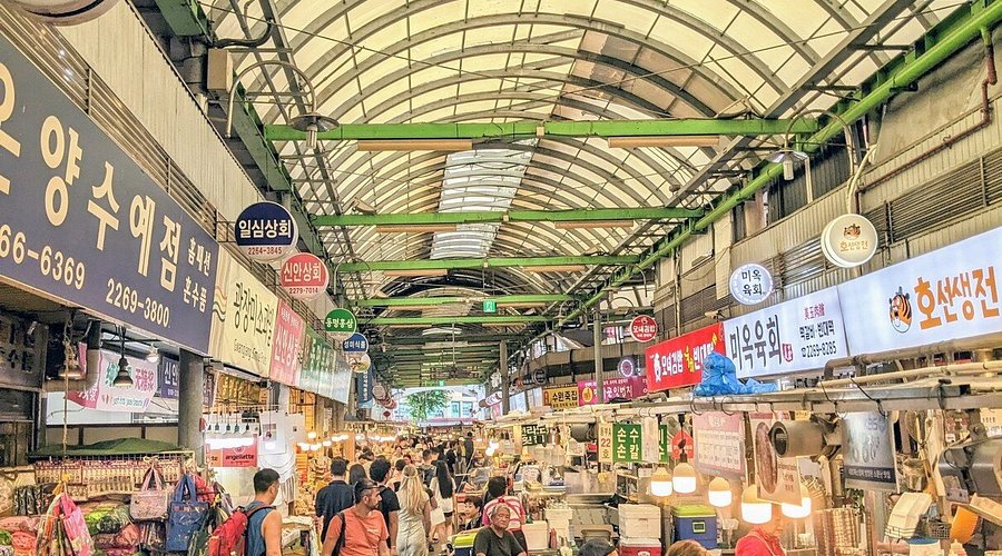 A crowded covered walkway at Gwangjang Market lined with food stalls and shop signs