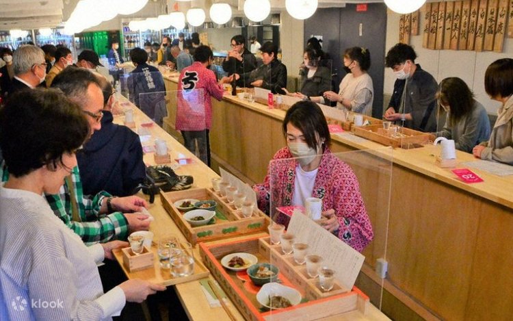 Visitors sampling sake at a tasting counter inside a Nada district brewery