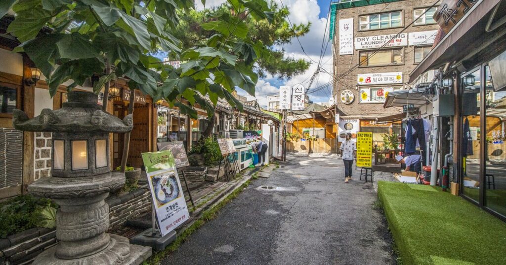 A narrow Seoul alley lined with shops, a stone lantern and hanging signage