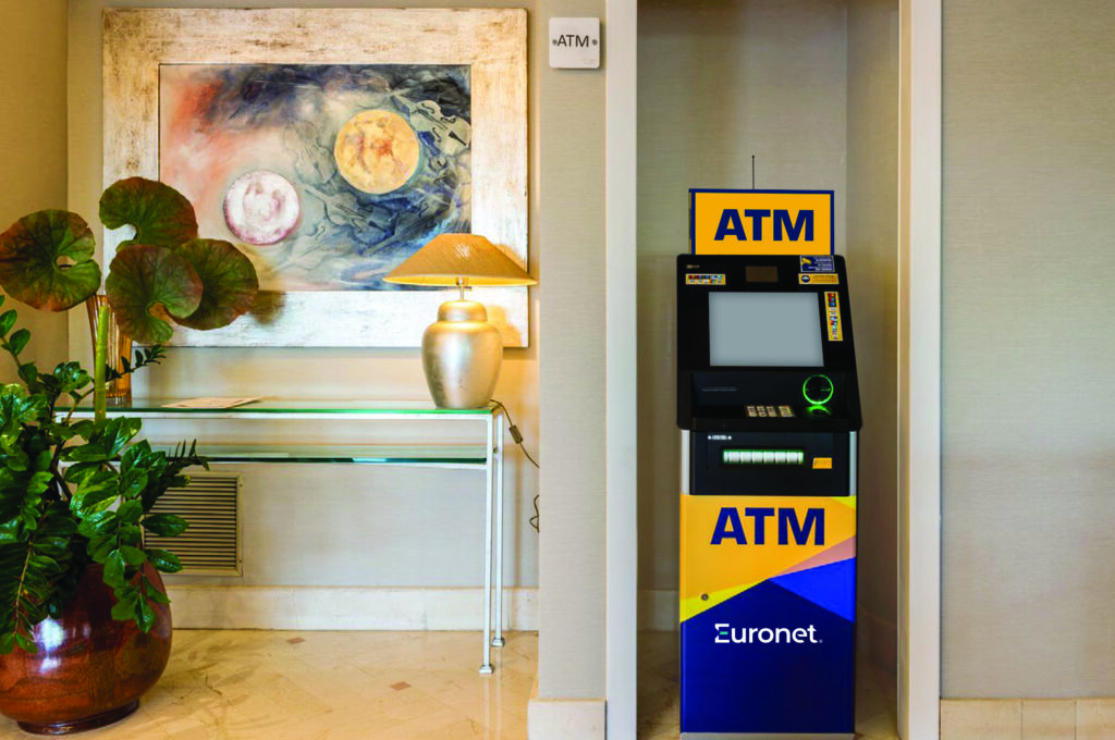 A blue and yellow Euronet ATM standing in a hotel lobby beside a console table