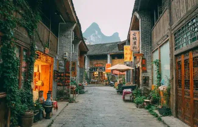A cobbled street in Xingping Ancient Town lined with old shophouses, a karst peak visible ahead
