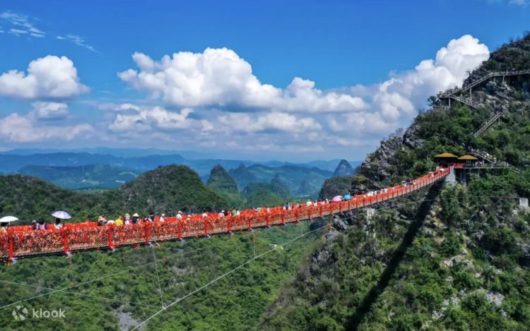 Visitors crossing a red suspension bridge strung with ribbons at Ruyi Peak