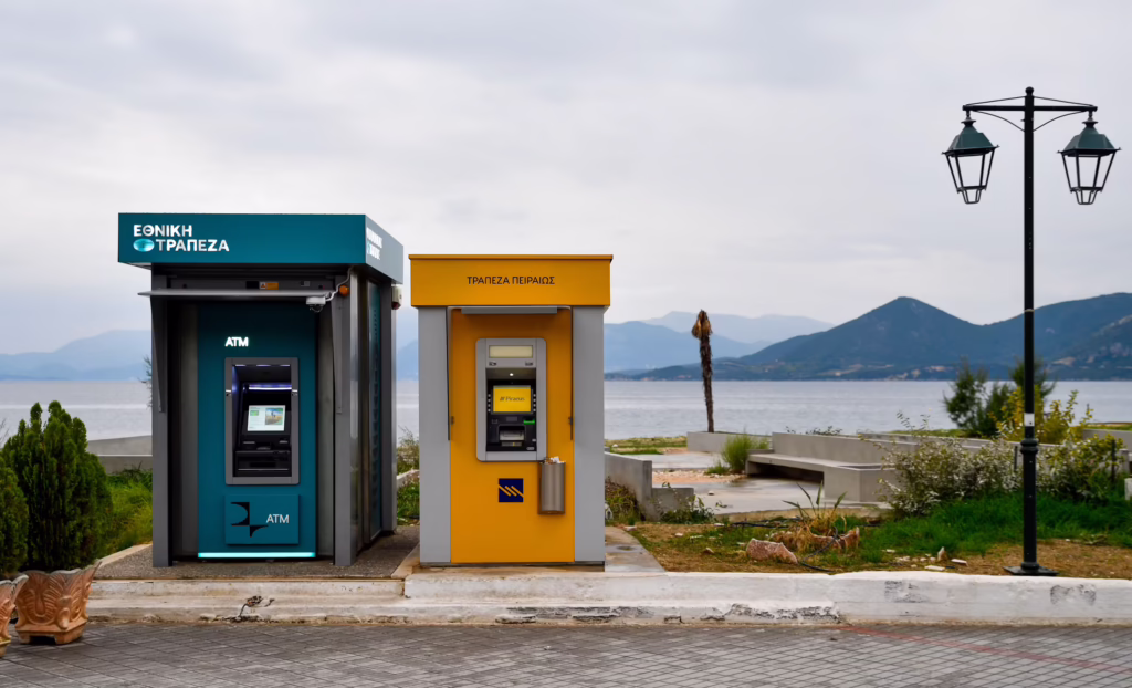 Roadside ATM kiosks for National Bank of Greece and Piraeus Bank on a Greek coastal street