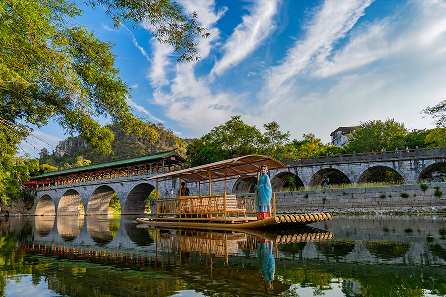 An old stone arched bridge over the river at Seven Star Park, a bamboo raft passing beneath
