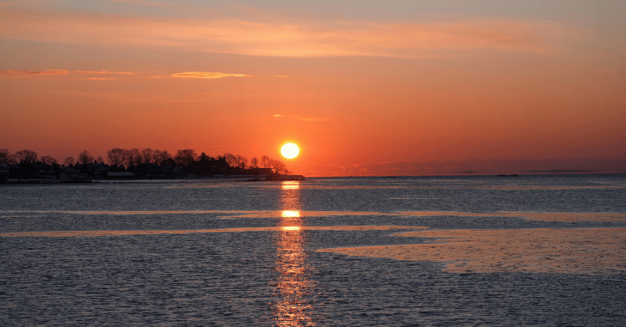 Sunset over a calm coastal bay, sun low on the horizon