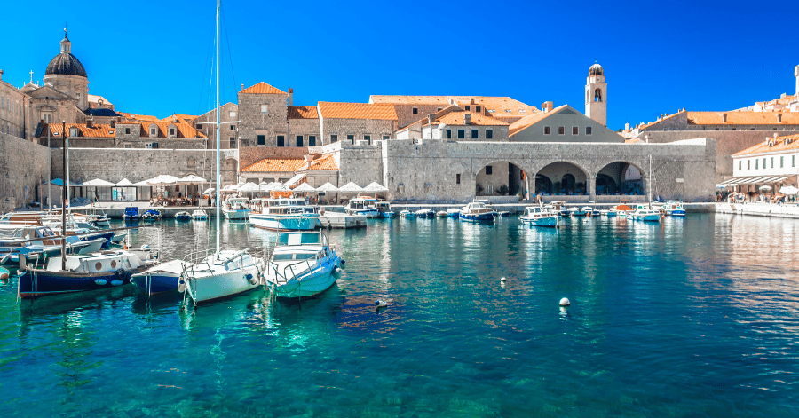 A Mediterranean harbour town with stone buildings, a bell tower and moored boats