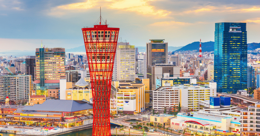 Kobe Port Tower rising above the city skyline at dusk with mountains behind