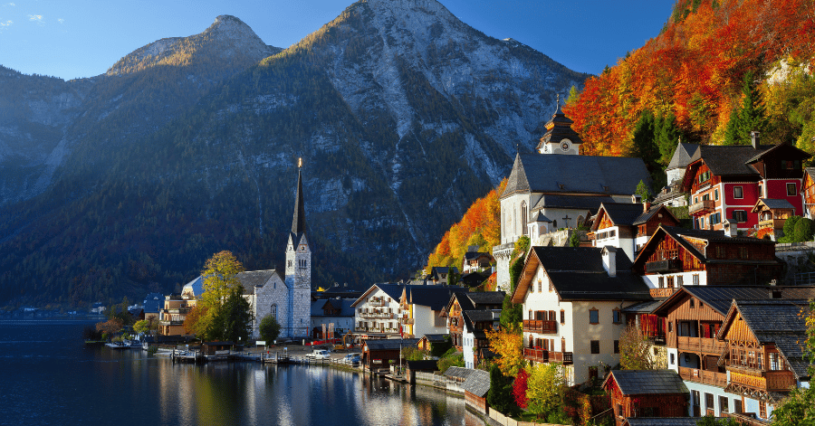 Hallstatt village and church spire on the lakeshore below mountains in autumn colour