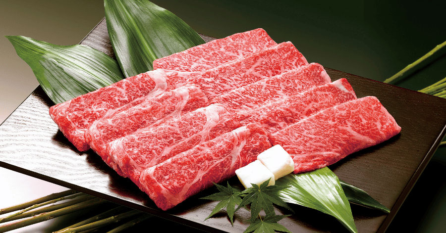 Raw sliced Kobe beef showing heavy white marbling, plated with bamboo leaves