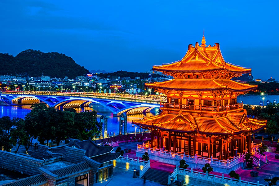 A tiered pagoda tower lit gold at night beside a bridge over the water
