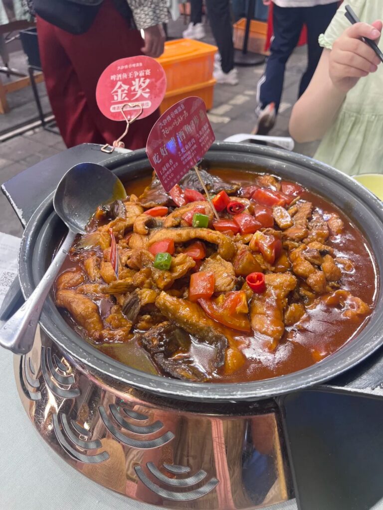 Beer fish braised with tomato and chilli in a metal claypot, an award tag hanging from the pot