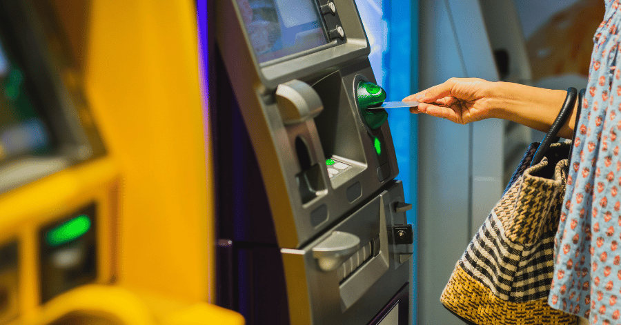 A hand inserting a card into an ATM beside a woven handbag