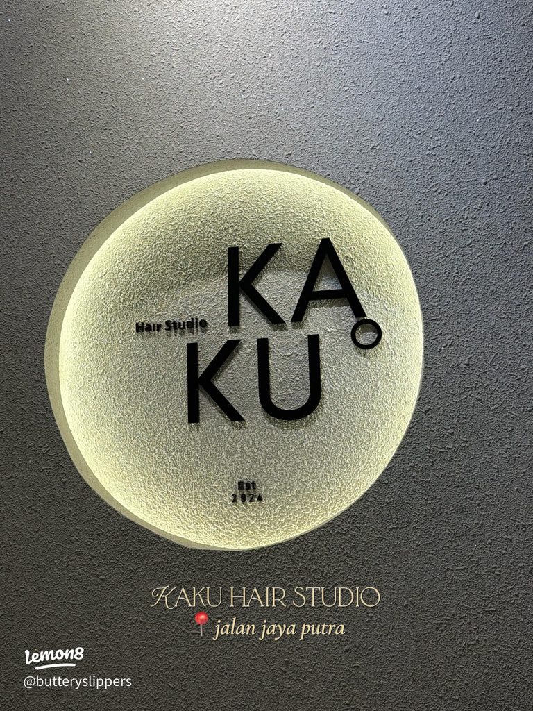 Kaku Hair Studio's circular backlit logo plaque on a textured grey wall