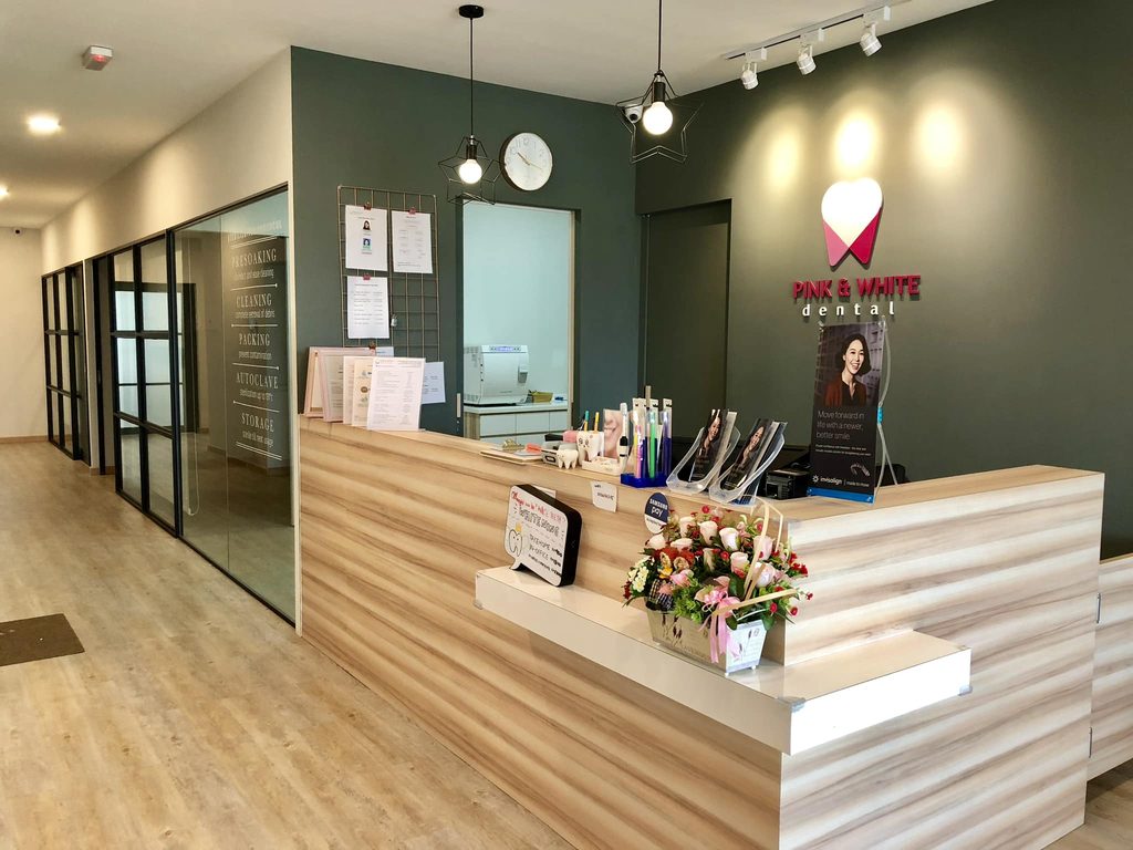 Reception counter at Pink & White Dental with a wood-grain front, flowers and the clinic logo on a green wall