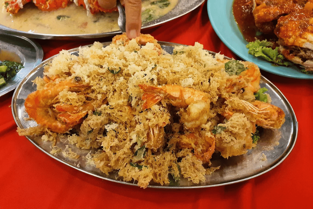 A platter of fried crispy prawns with live crab curry in the background at Selera Senibong Seafood