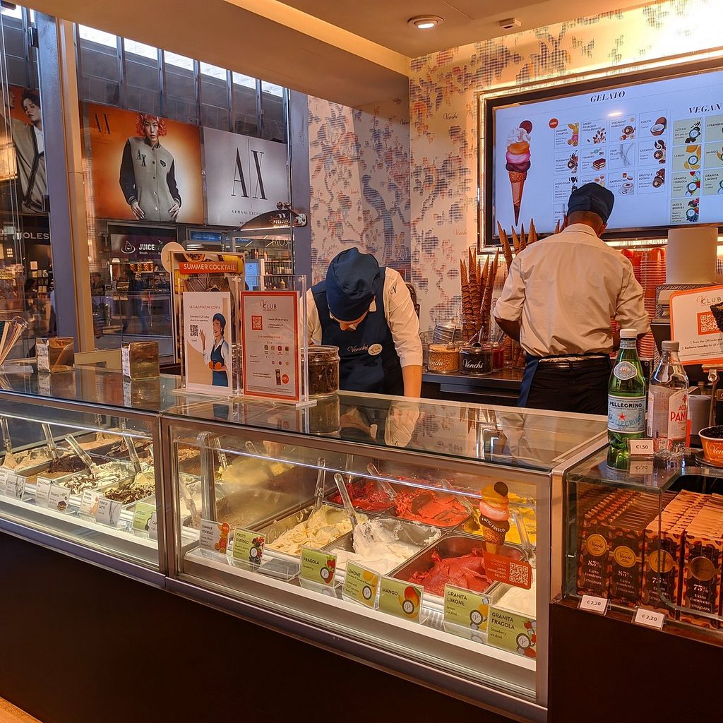 A server scooping gelato behind the counter at a Venchi gelateria