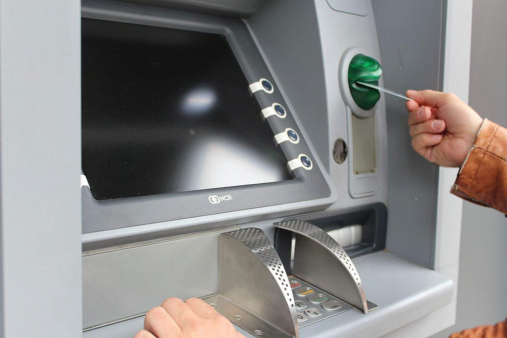 A hand inserting a debit card into an ATM machine's card slot