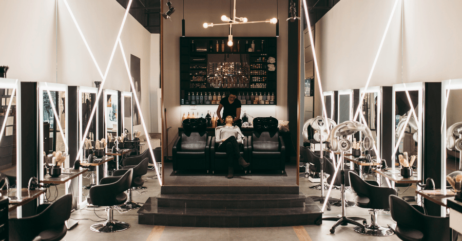 A dimly-lit salon styling area with mirrored stations and a wash chair in the centre
