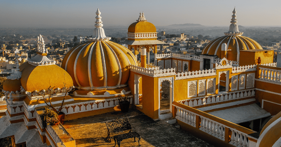 Golden domes of a rooftop palace overlooking an Indian city at sunset