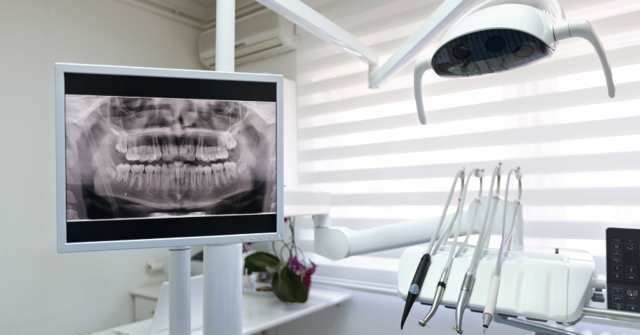 Panoramic dental X-ray of a full set of teeth on a monitor beside a dental chair light and handpieces