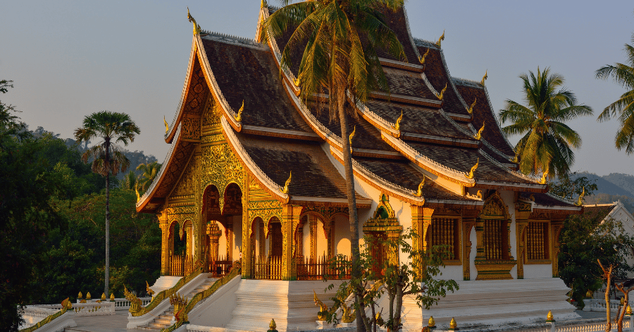 Haw Pha Bang's gilded multi-tiered roof at Luang Prabang's Royal Palace, framed by palm trees at golden hour