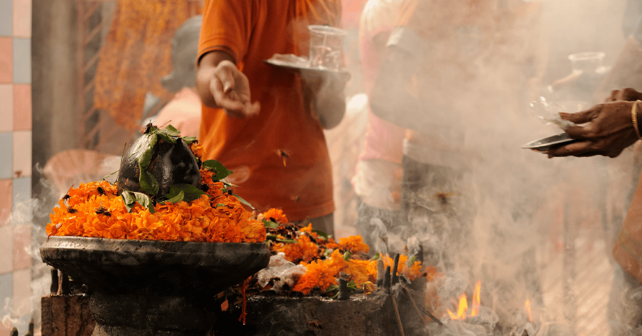 A priest making a puja offering with marigold flowers and incense at an Indian temple