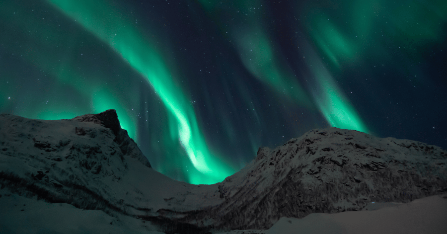 Northern lights streaking across the night sky above snow-covered mountains